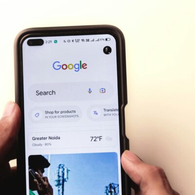 A close-up of a hand holding a smartphone with Google search displayed on the screen.